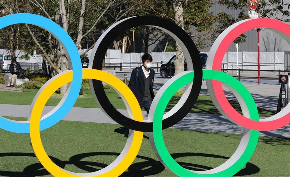 a pedestrian wearing mask walking past the Olympic rings in Tokyo Japan