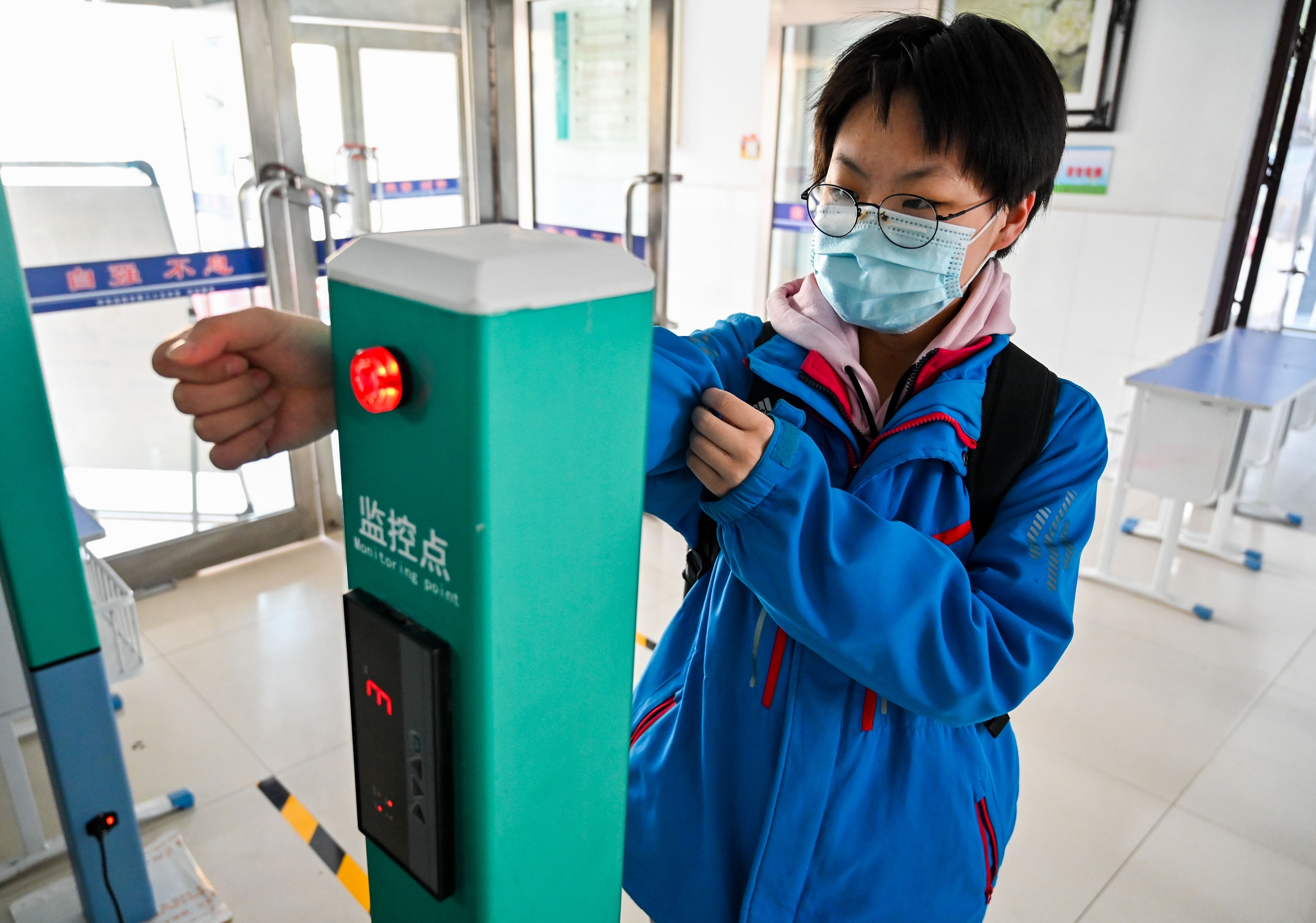 A graduating student gets temperature checked at the entrance of the school building