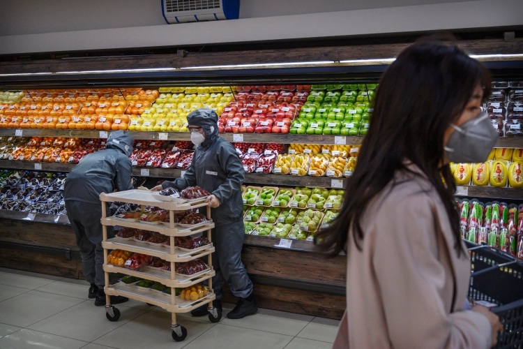 Chinese workers wear protective suits and masks as they stock fruit at a supermarket