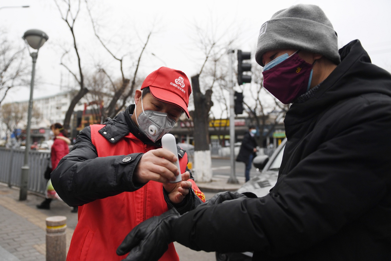 Volunteer Zhang Jianguo L takes the temperature of a resident at the entrance of Cheniandian Lane in Beijing
