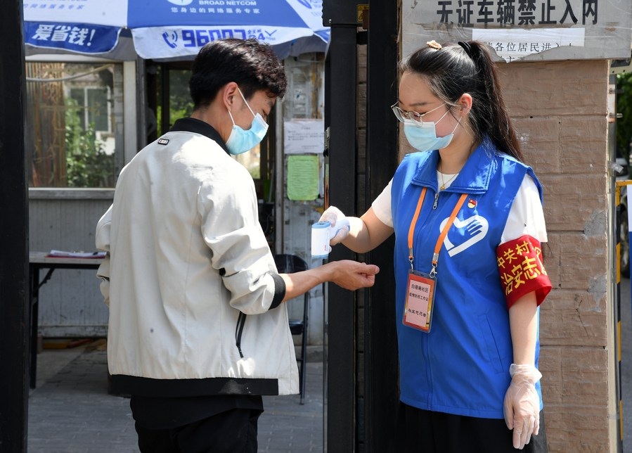Volunteer Wang Yue R checks a residents body temperature at the entrance of a community in Haidian District in Beijing capital of China
