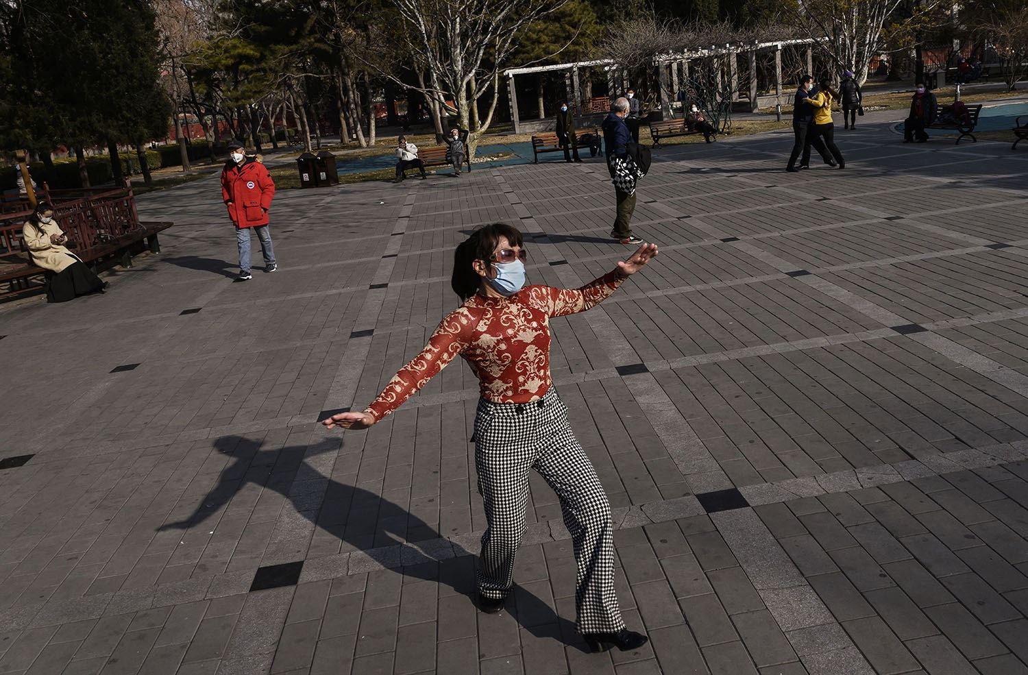 A Chinese woman wears a protective mask as she dances in a sparsely attended park in Beijing