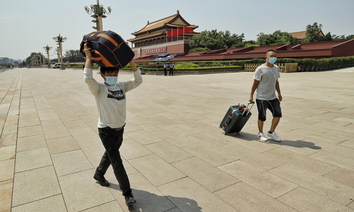 Two men in masks carry luggage pass Tiananmen Square
