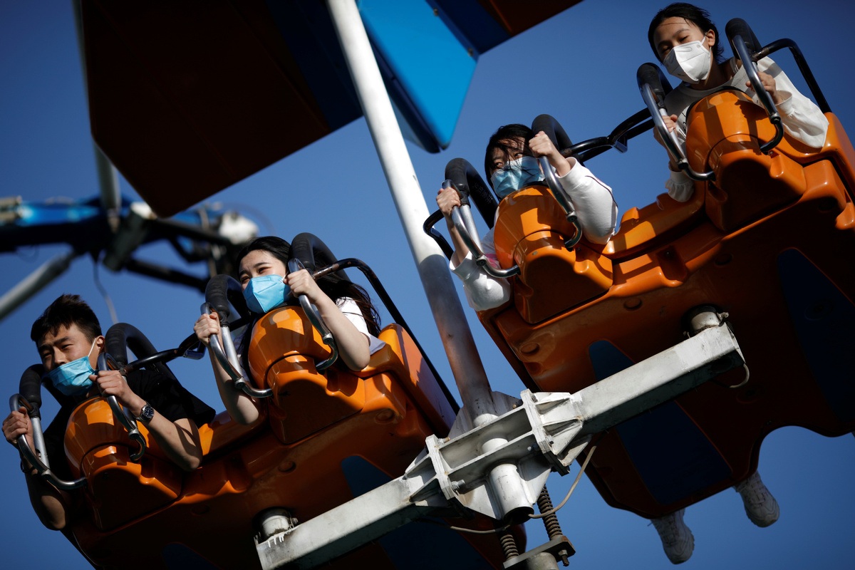 People wearing face masks enjoy an attraction at the Happy Valley amusement park in Beijing