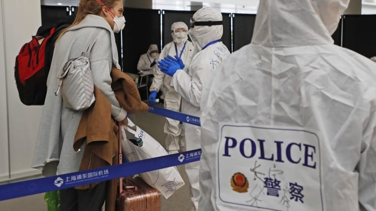 Police officers wearing protective suits check information of an inbound passenger at airport