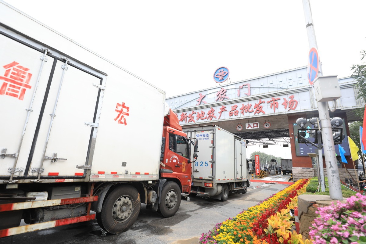 Trucks loaded with fruit and vegetables drive through the Xinfadi market gate on the morning of Aug 15