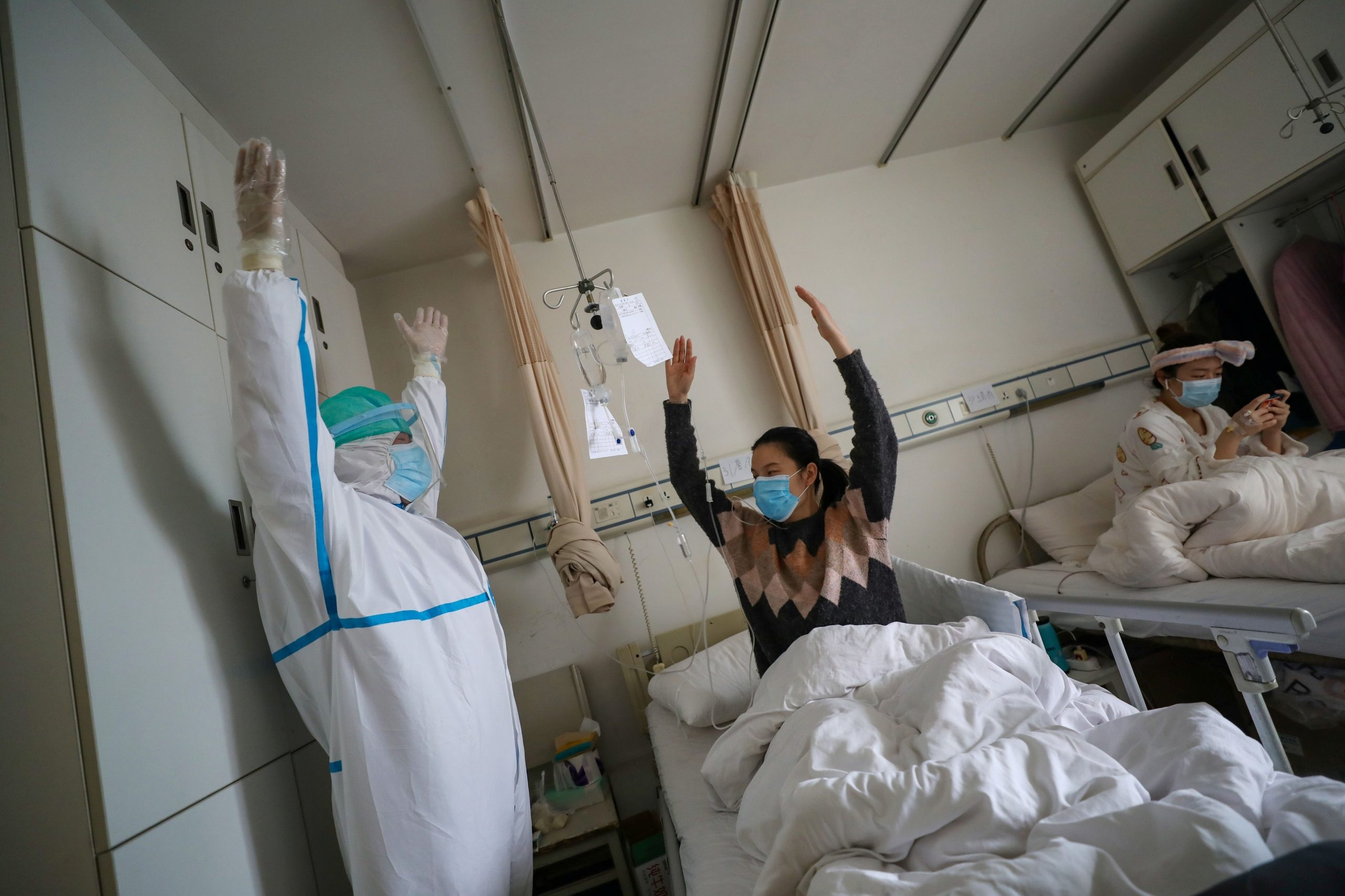 A medical worker in a protective suit shows a patient gestures of an exercise for rehabilitation at a ward of Wuhan Red Cross Hospital in Wuhan