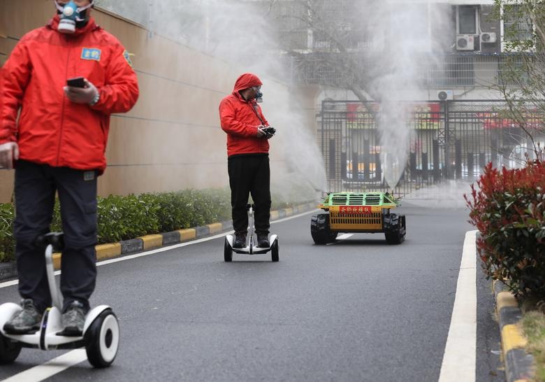 Workers ride smart self balancing scooters as they control a robotic sprayer spraying disinfectant at a residential compound in Wuha