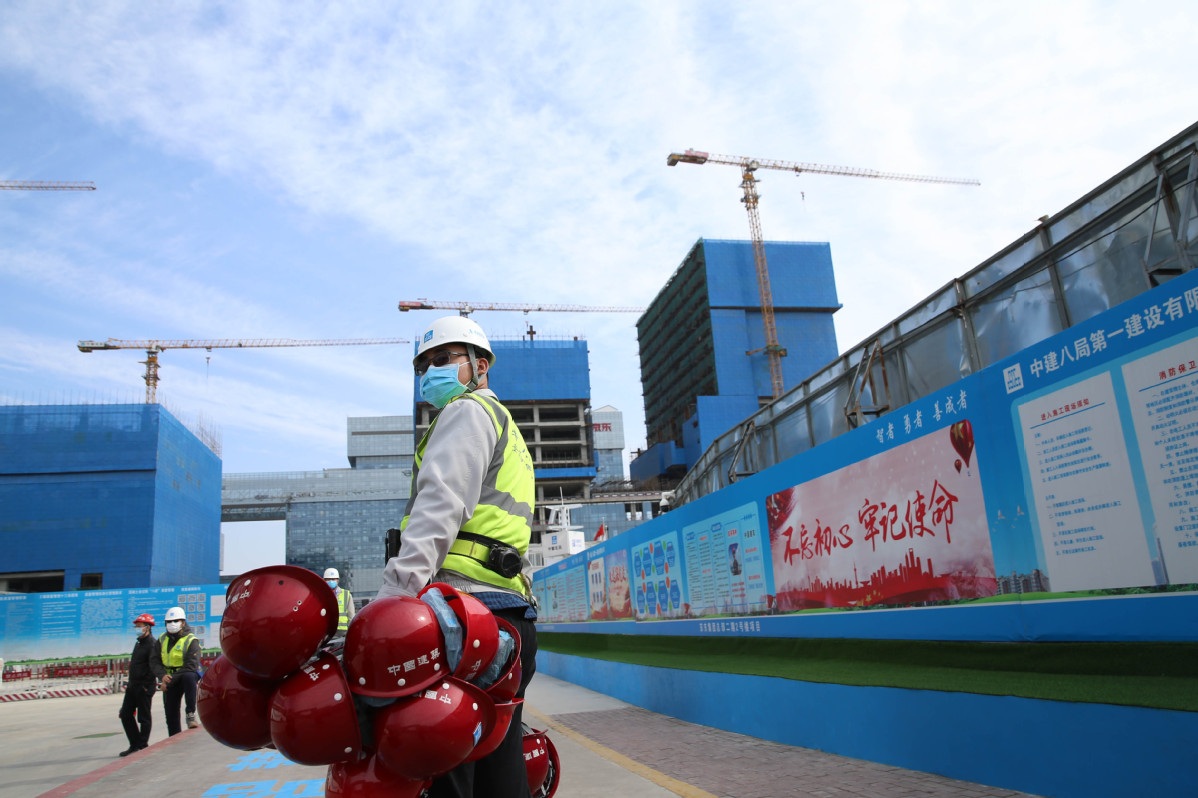 A construction worker carries hard hats on a site in Beijing